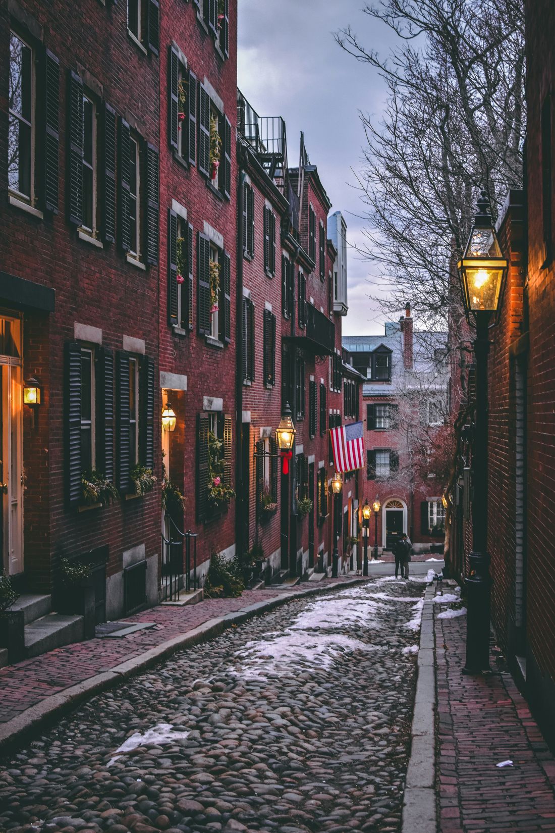 Brick rowhouses with gas lamps along a narrow cobblestone lane